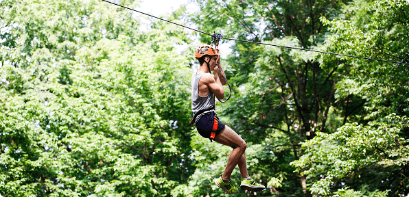 Visitor enjoying a high zip line ride through lush green trees at RushCliff’s adventure park zone.