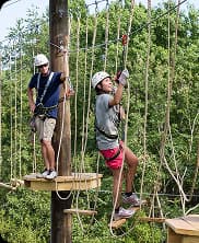 Two people climbing rope elements on a vertical challenge course designed for teamwork and courage.