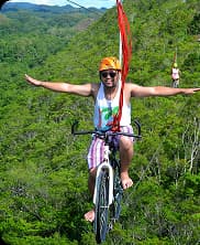Person riding a zip cycle high above the ground during an adventure relay activity in nature.