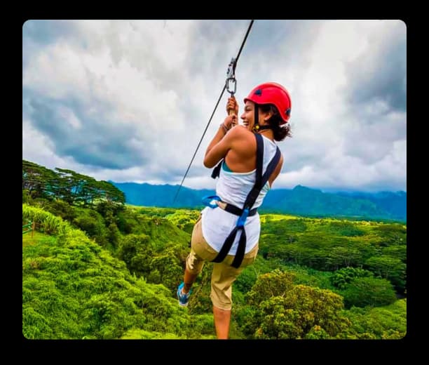 Person enjoying an exciting zipline ride high above a scenic green forest with mountains in the background