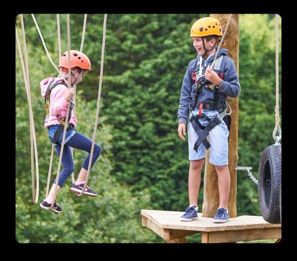 Two children wearing helmets enjoying a fun outdoor rope course activity in a green natural setting