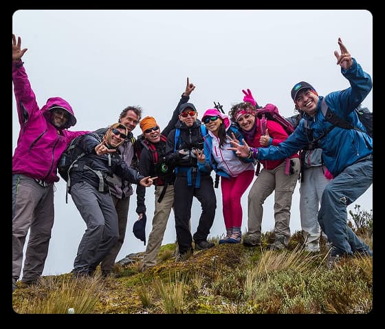 A cheerful group of trekkers raise their hands while posing on a mountain trail during a team adventure
