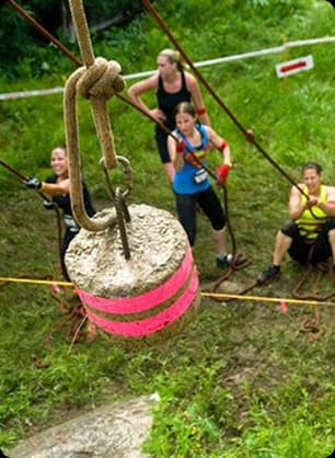 A group of teens work together on an outdoor leadership task involving ropes and a suspended object.