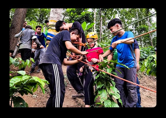 Group of students participating in a rope-based adventure activity in a forest setting with guidance