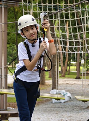 A young participant wearing safety gear navigates a rope obstacle course during an outdoor adventure event.